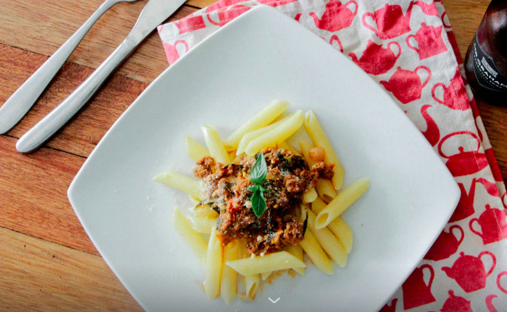 A square plate with some Quorn meat and pasta on it, placed on a tea towel with red kettles on.